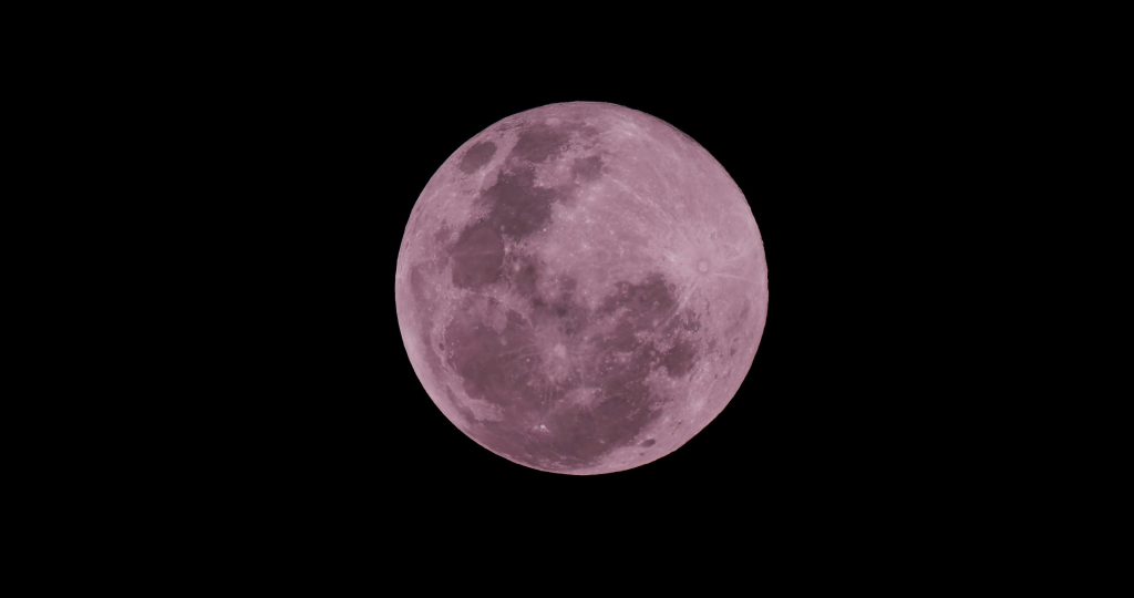 A beautifully captured pink full moon in the clear night sky over Toledo, Spain.