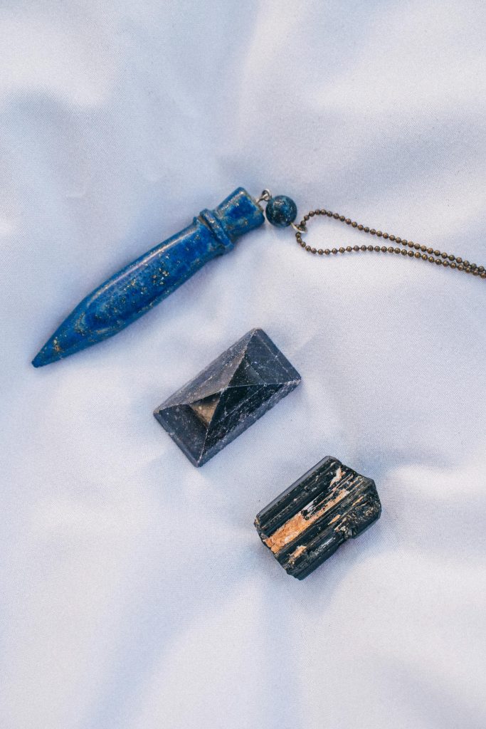 Lapis Lazuli Top view of healing crystals including a pendulum, pyramid, and raw tourmaline on a soft white cloth.