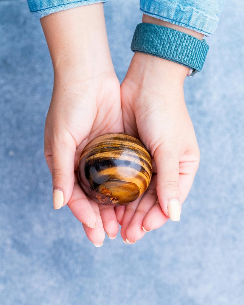 Tiger's eye Close-up of hands gently cradling a polished tiger's eye stone sphere against a blue background.