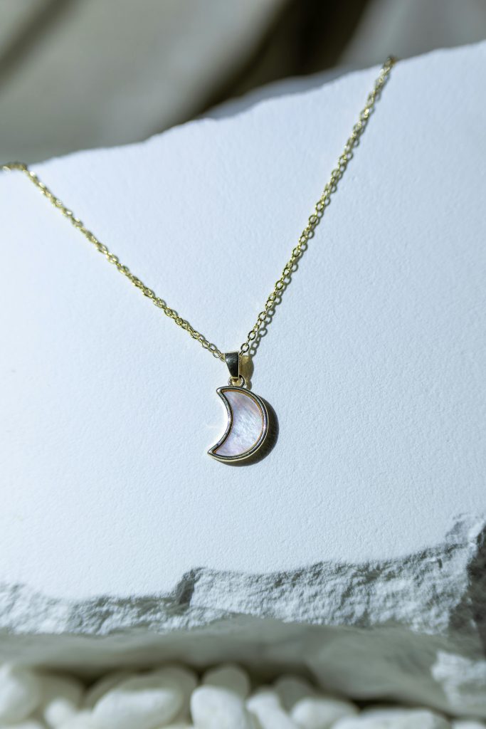 A close-up of a crescent moon pendant on a gold chain displayed on a white surface.